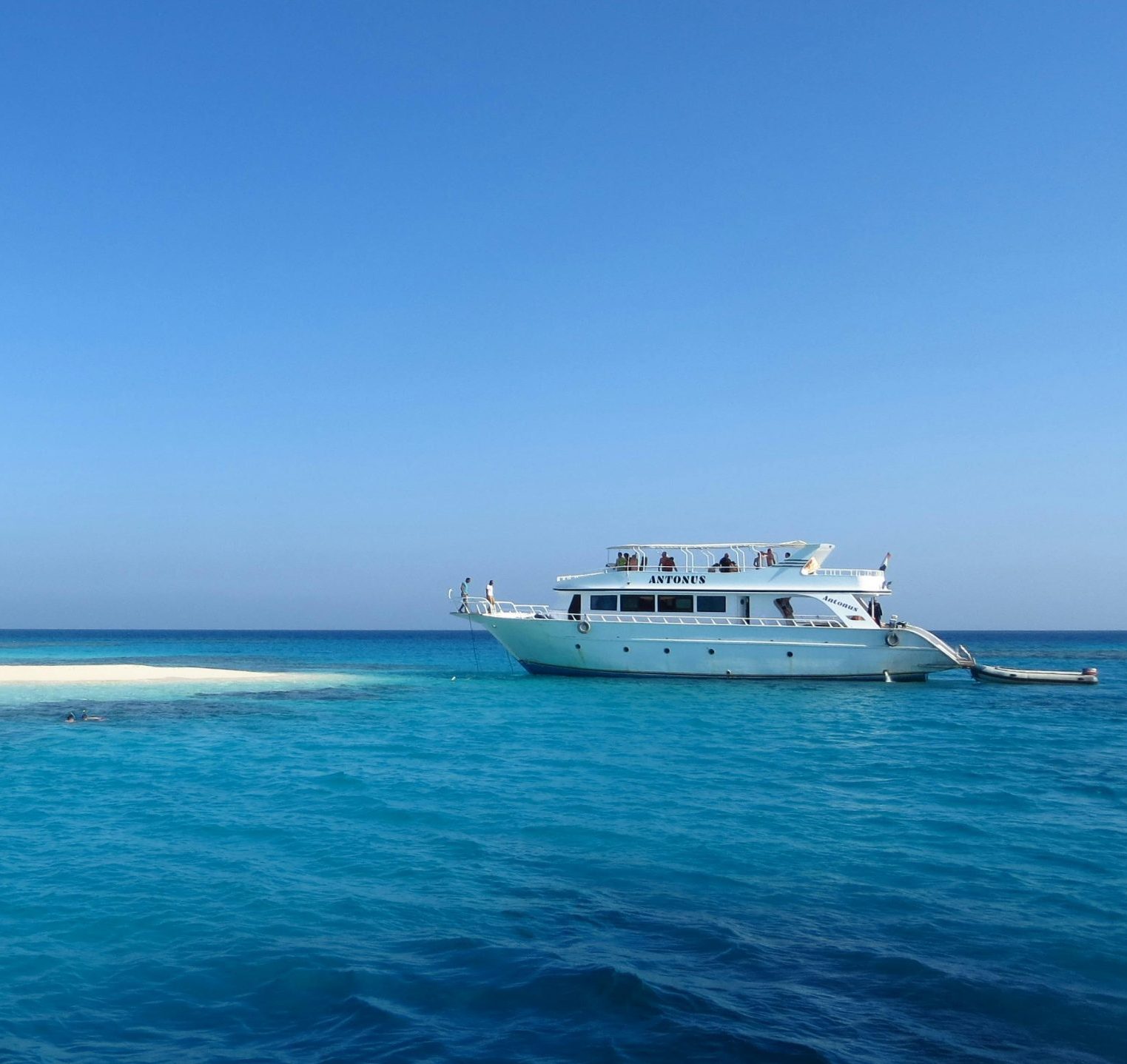 A scenic view of a luxury yacht by a pristine, sandy island in Egypt's vibrant blue waters.Hani- travel - резервирайте lux- аранжмани Hugrada Egipet, all inclusive , пирамиди